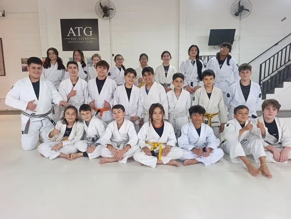 Turma Kids e juvenil da ATG Jiu-Jitsu Itatiba posada no tatame, embaixo da placa da academia